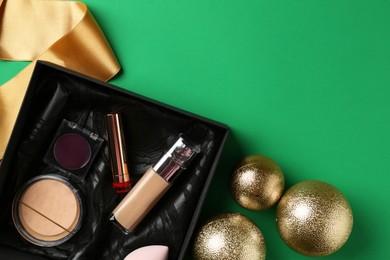 Christmas present. Decorative cosmetics in gift box and festive balls on green background, flat lay