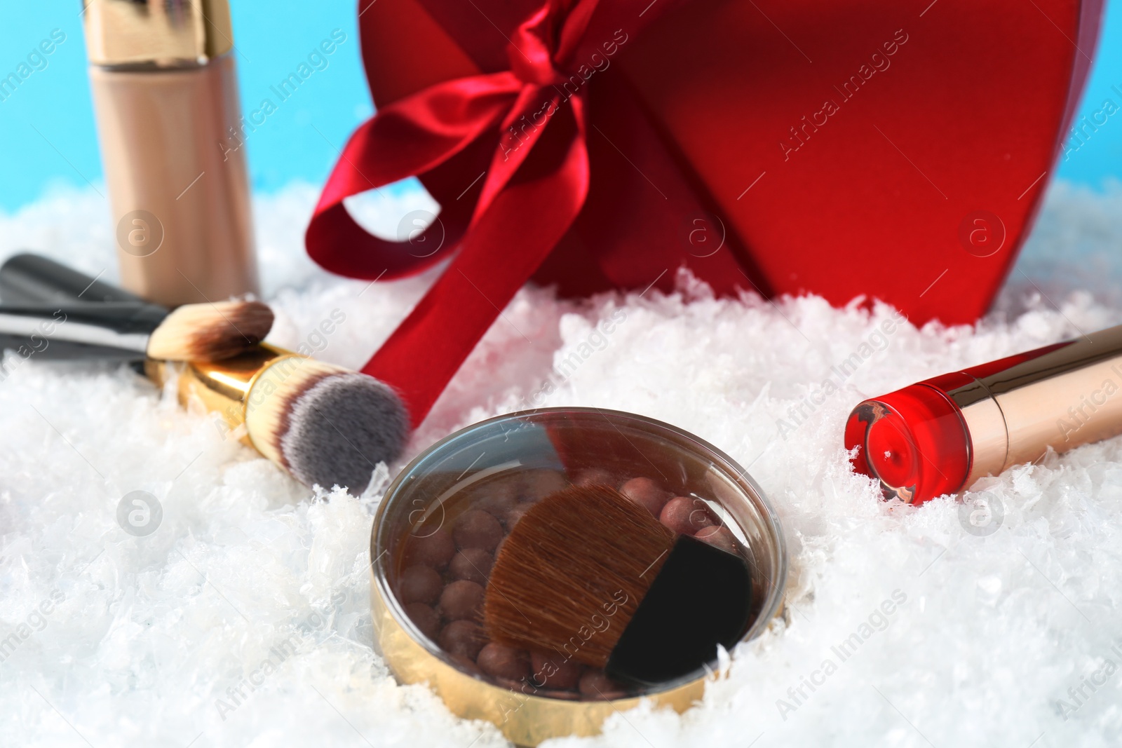 Photo of Christmas present. Decorative cosmetics and gift box on snow against light blue background, closeup