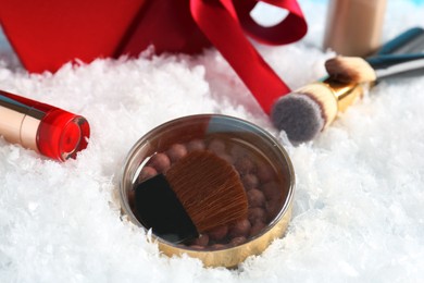 Photo of Christmas present. Decorative cosmetics and makeup brushes on snow, closeup