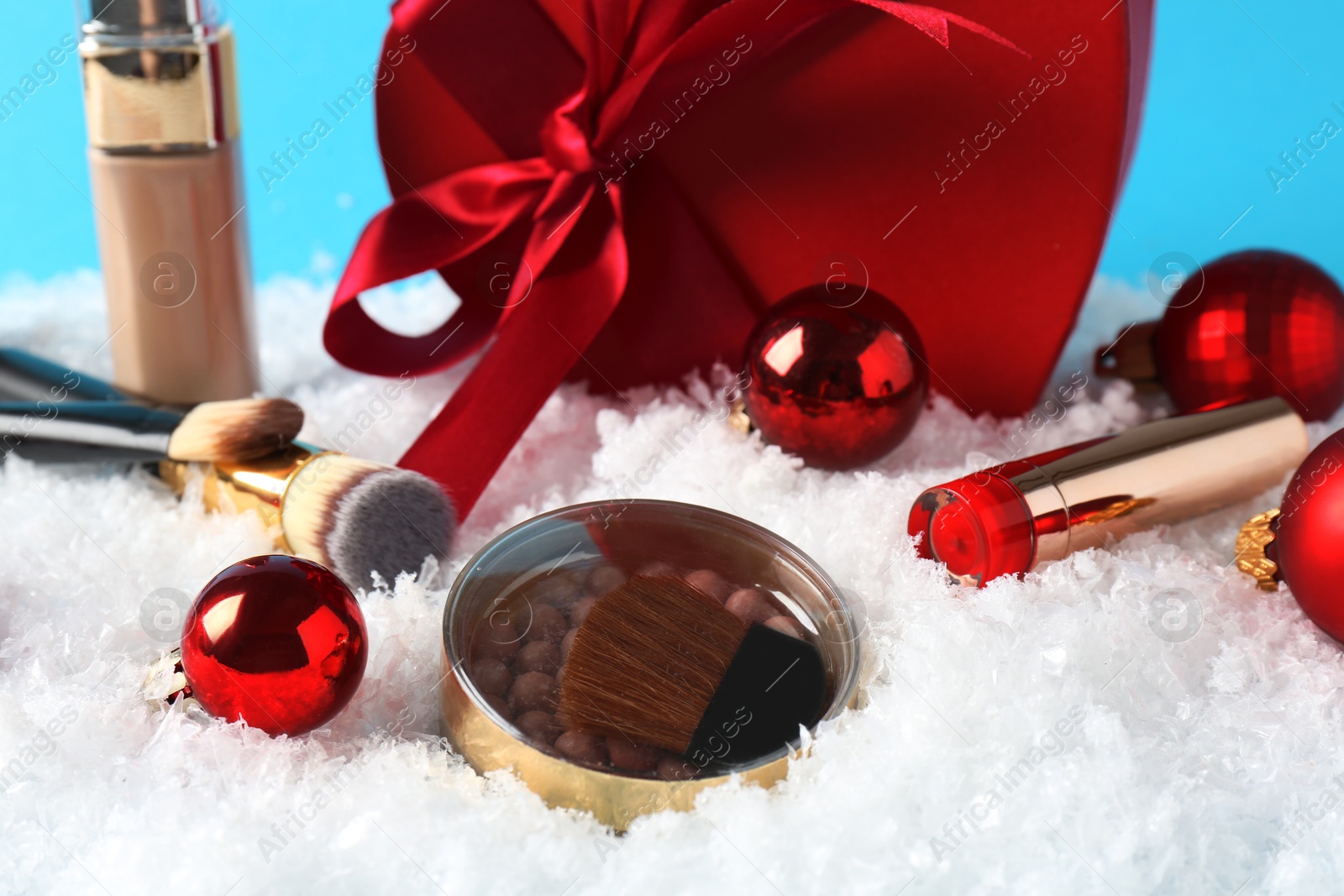 Photo of Christmas present. Decorative cosmetics and gift box on snow against light blue background, closeup