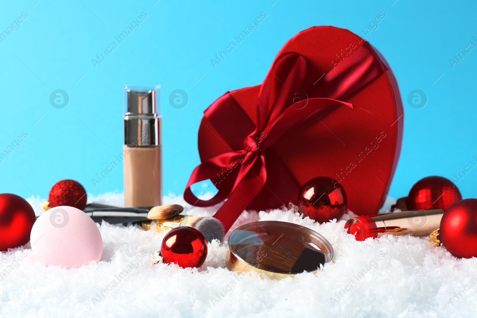 Photo of Christmas present. Decorative cosmetics and gift box on snow against light blue background