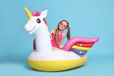 Photo of Happy little girl in beachwear with inflatable unicorn shaped ring on light blue background