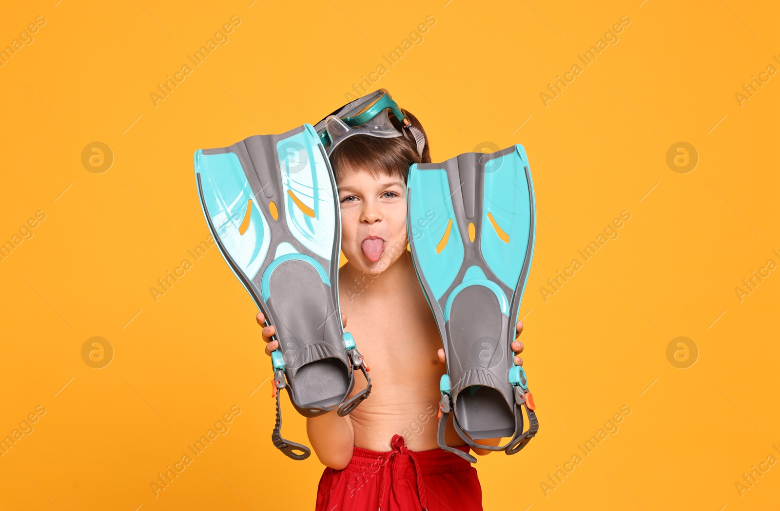 Photo of Little boy in beachwear with diving mask and flippers on orange background