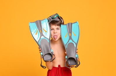 Little boy in beachwear with diving mask and flippers on orange background