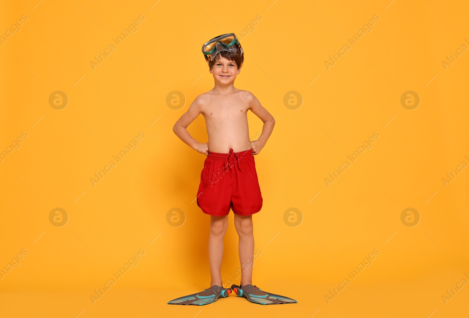 Photo of Little boy in beachwear with diving mask and flippers on orange background