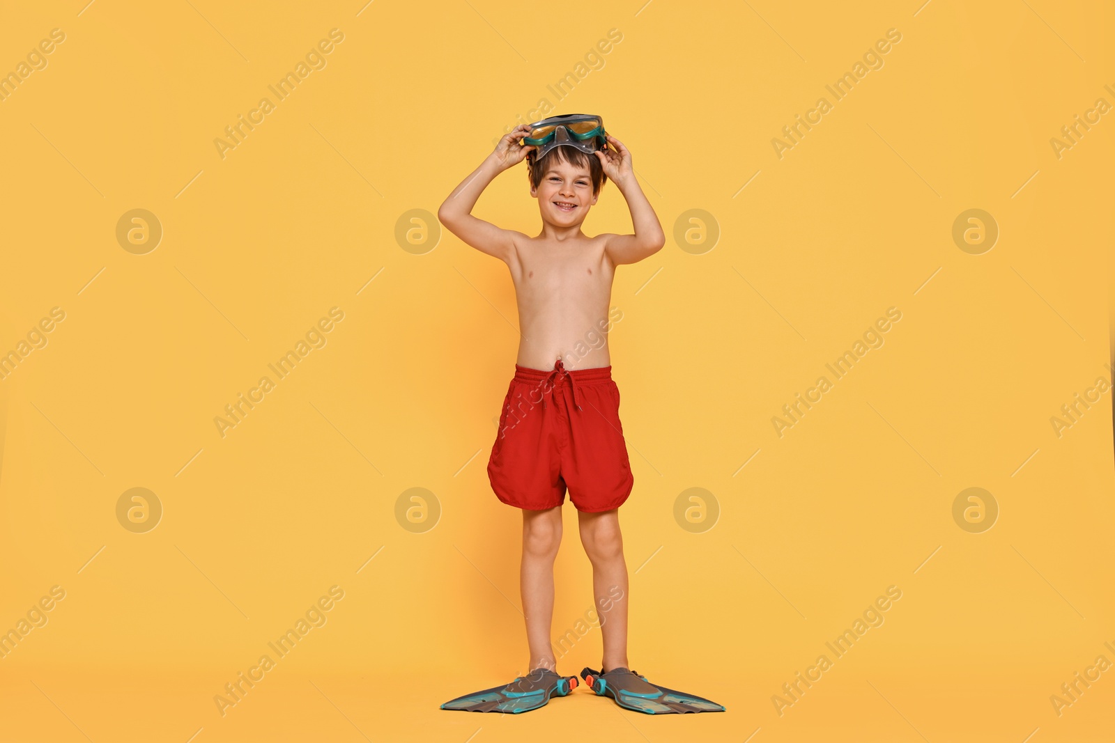 Photo of Little boy in beachwear with diving mask and flippers on orange background