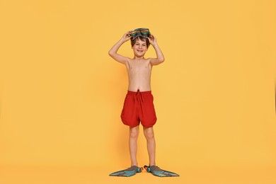 Little boy in beachwear with diving mask and flippers on orange background