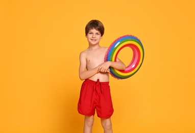 Photo of Happy little boy in beachwear with inflatable ring on orange background