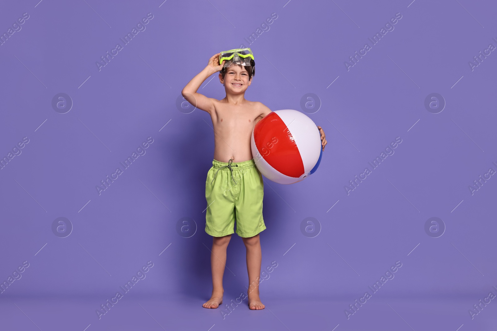 Photo of Little boy in beachwear with diving mask and inflatable ball on purple background