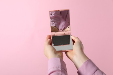 Woman holding pocket mirror on pink background, closeup