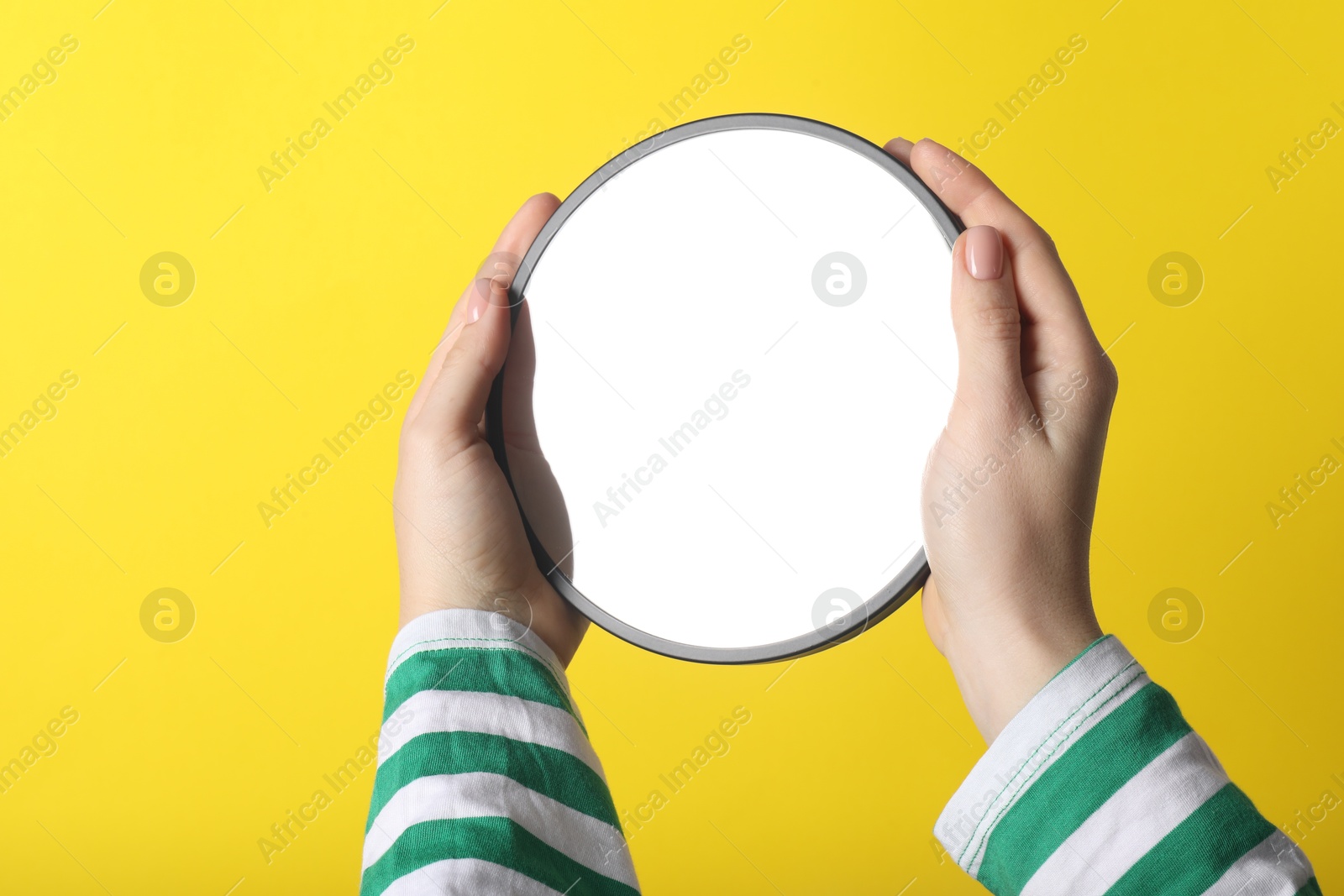 Photo of Woman holding round mirror on yellow background, closeup