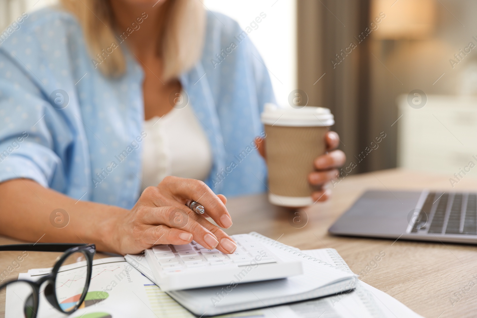 Photo of Budget planning. Woman with coffee using calculator at table indoors, closeup