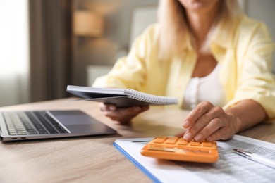 Photo of Budget planning. Woman with notebook using calculator at table indoors, closeup