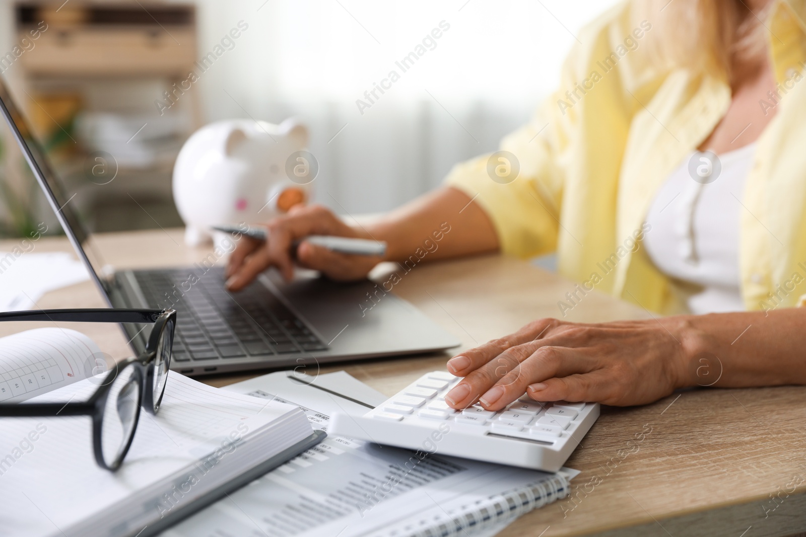 Photo of Budget planning. Woman working on laptop while using calculator at table indoors, closeup