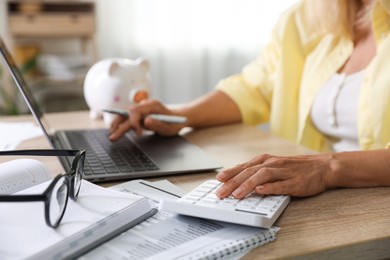 Photo of Budget planning. Woman working on laptop while using calculator at table indoors, closeup