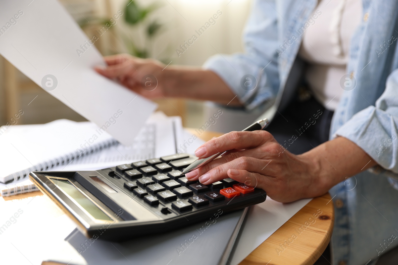 Photo of Budget planning. Woman using calculator while working with accounting document at table indoors, closeup