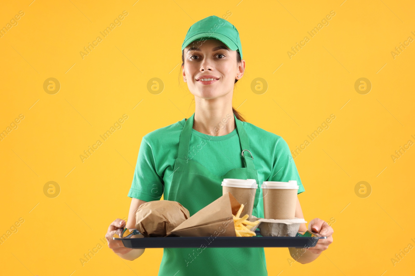 Photo of Fast-food worker holding tray with order on orange background