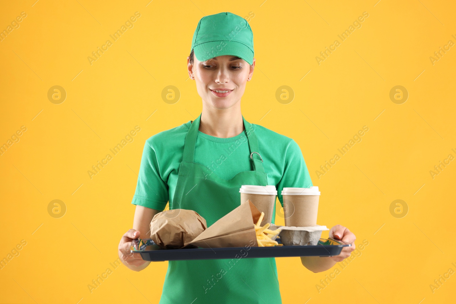 Photo of Fast-food worker holding tray with order on orange background