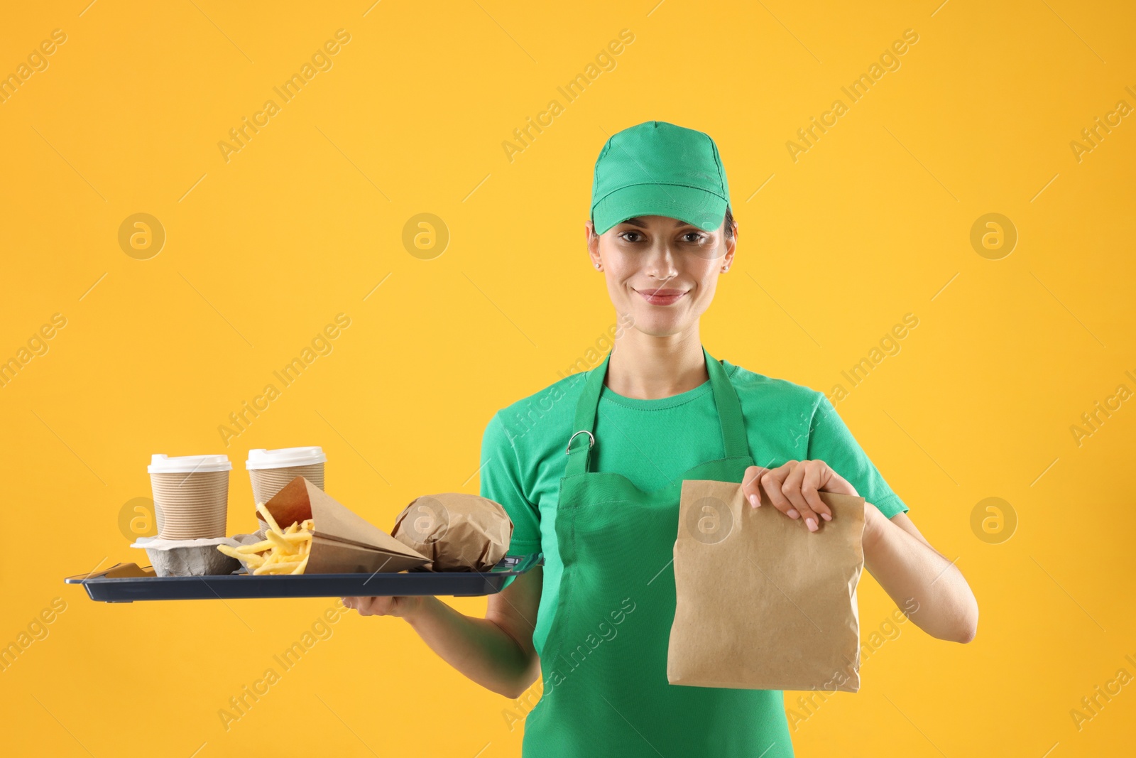 Photo of Fast-food worker holding tray with order on orange background