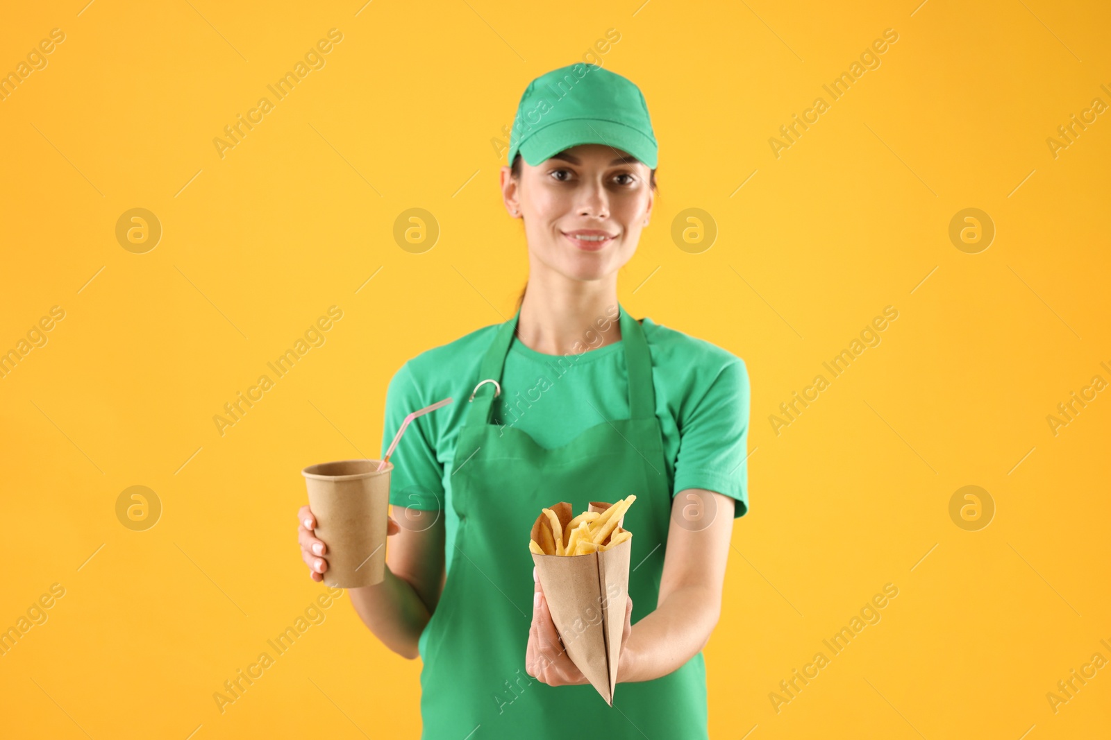 Photo of Fast-food worker with French fries and paper cup on orange background