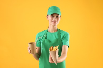 Photo of Fast-food worker with French fries and paper cup on orange background