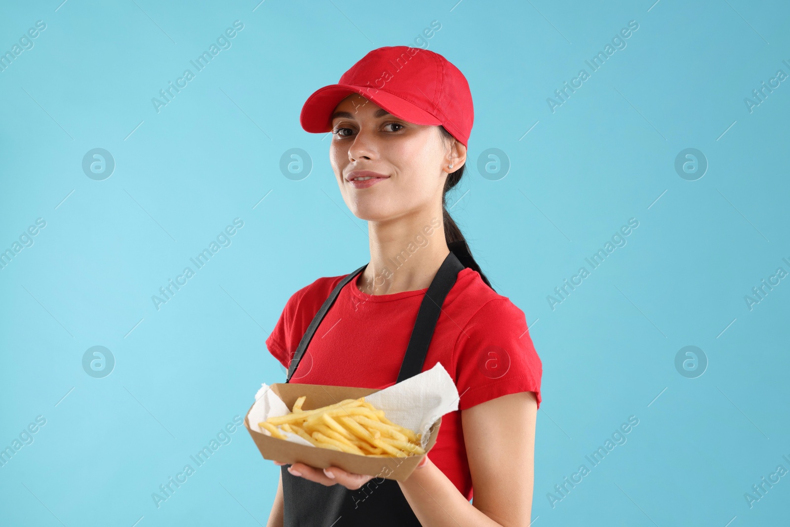 Photo of Fast-food worker holding paper container with fries on light blue background