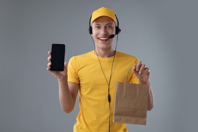 Photo of Fast-food worker with paper bag and smartphone on gray background