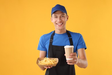 Photo of Fast-food worker holding paper container with fries and cup on orange background