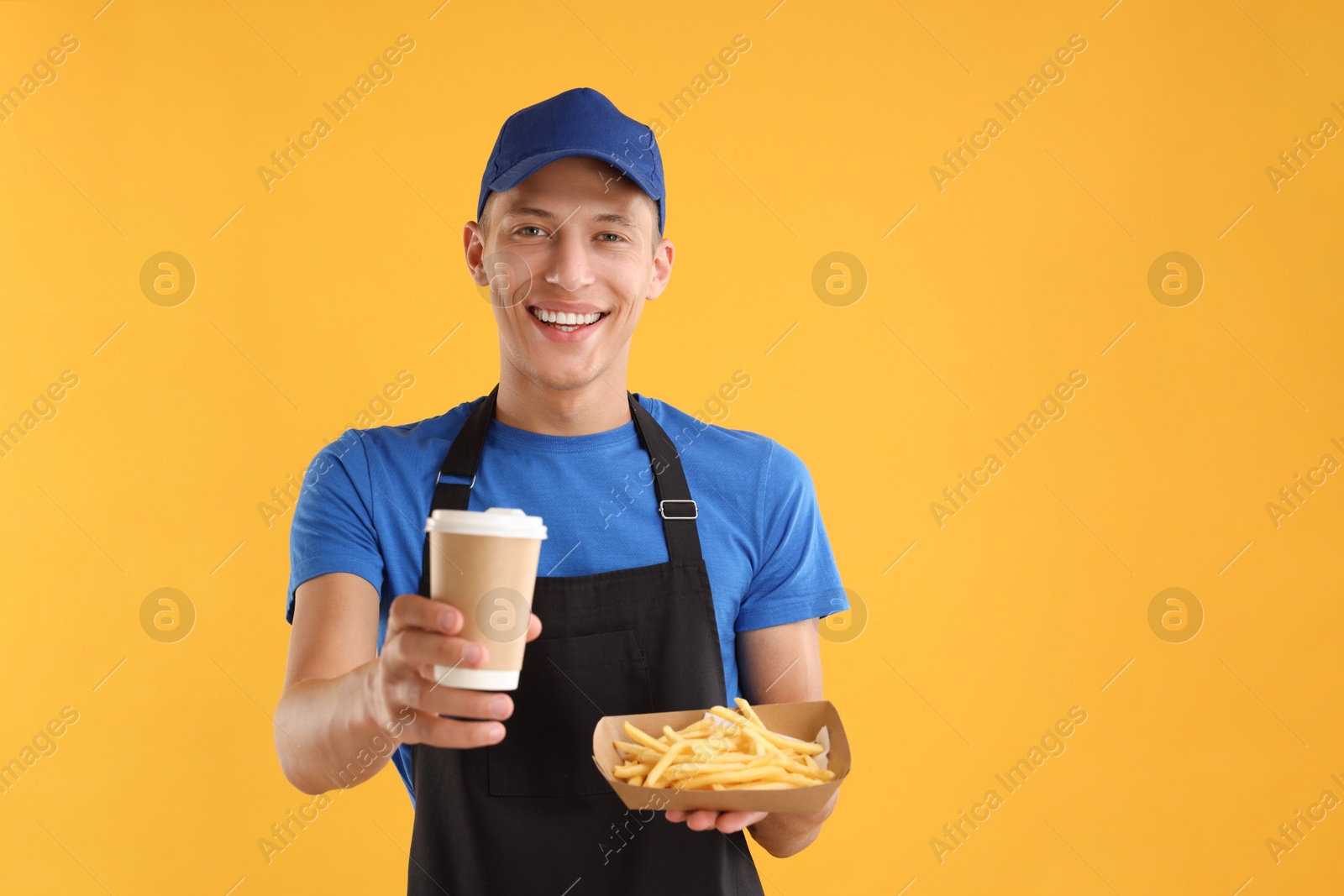 Photo of Fast-food worker holding paper container with fries and cup on orange background