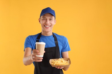 Photo of Fast-food worker holding paper container with fries and cup on orange background