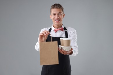 Photo of Fast-food worker with paper bag and cups on gray background