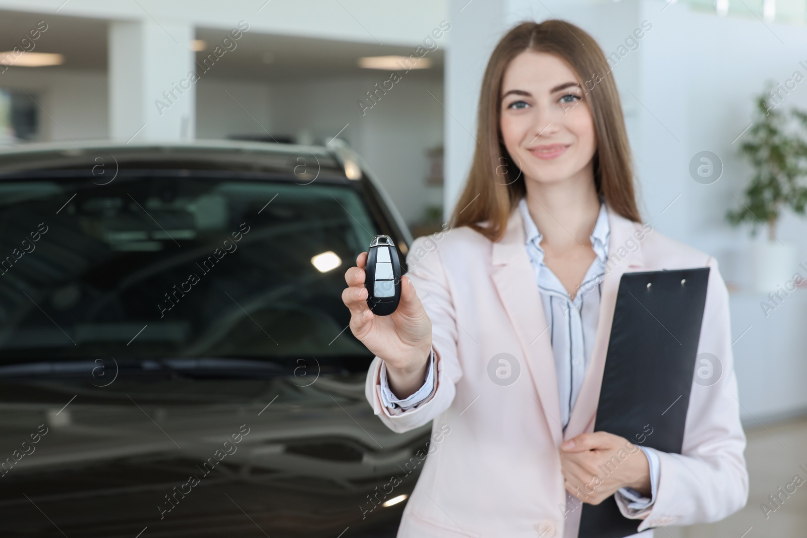 Photo of Happy saleswoman holding key near new black car in salon