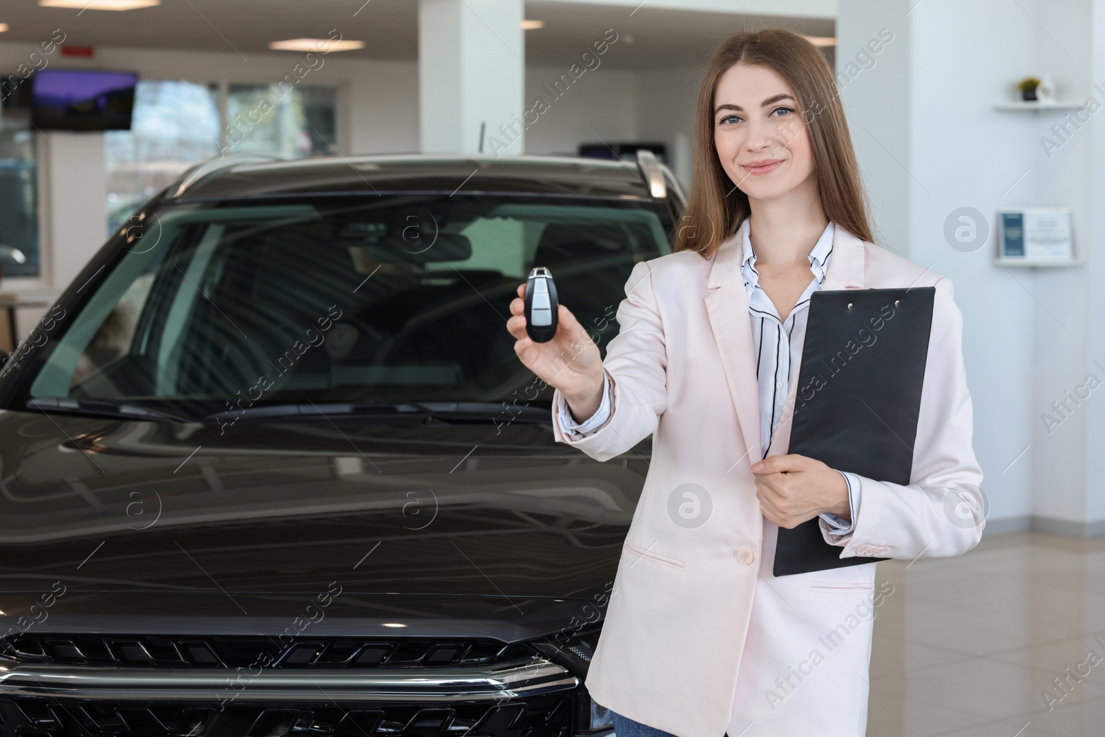 Photo of Happy saleswoman holding key near new black car in salon