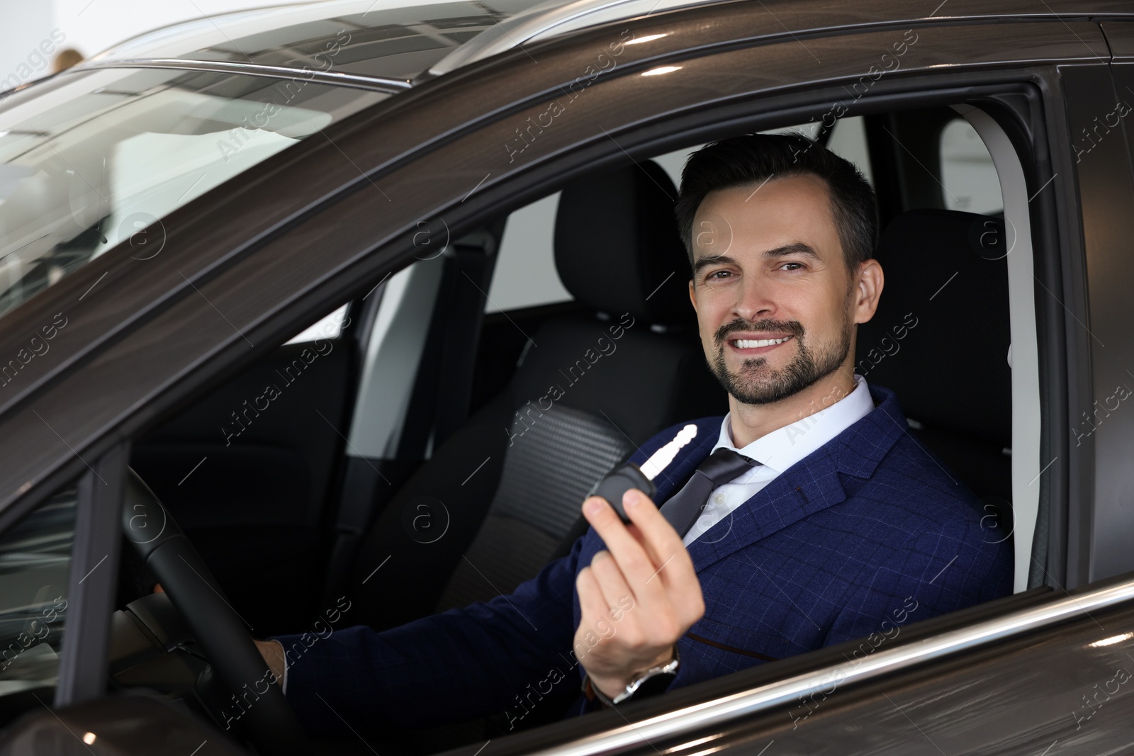 Photo of Happy salesman holding key inside new black car in salon