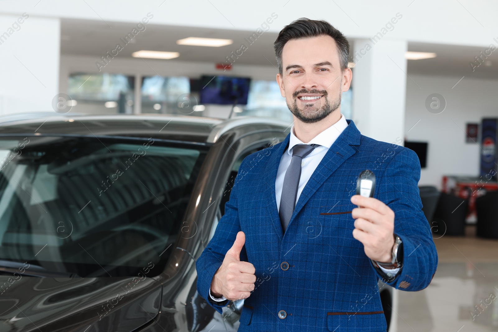 Photo of Happy salesman with car key showing thumbs up in salon