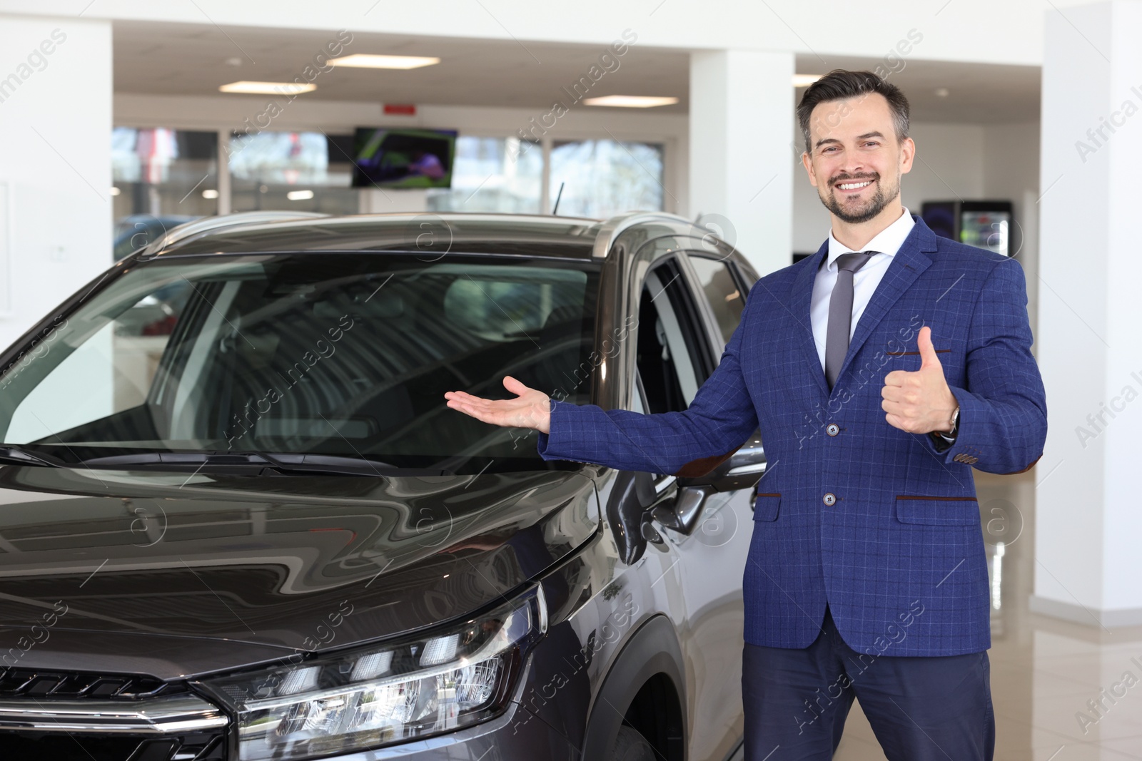 Photo of Happy salesman showing thumbs up near new black car in salon