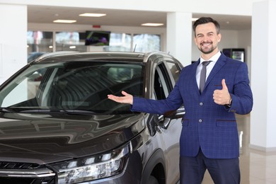 Photo of Happy salesman showing thumbs up near new black car in salon