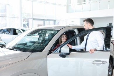 Photo of Happy salesman showing car to client in salon