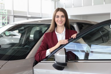 Photo of Happy saleswoman near new silver car in salon