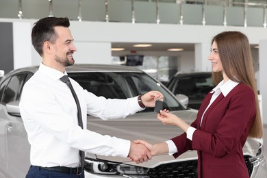 Photo of Salesman giving key to client near new car in salon