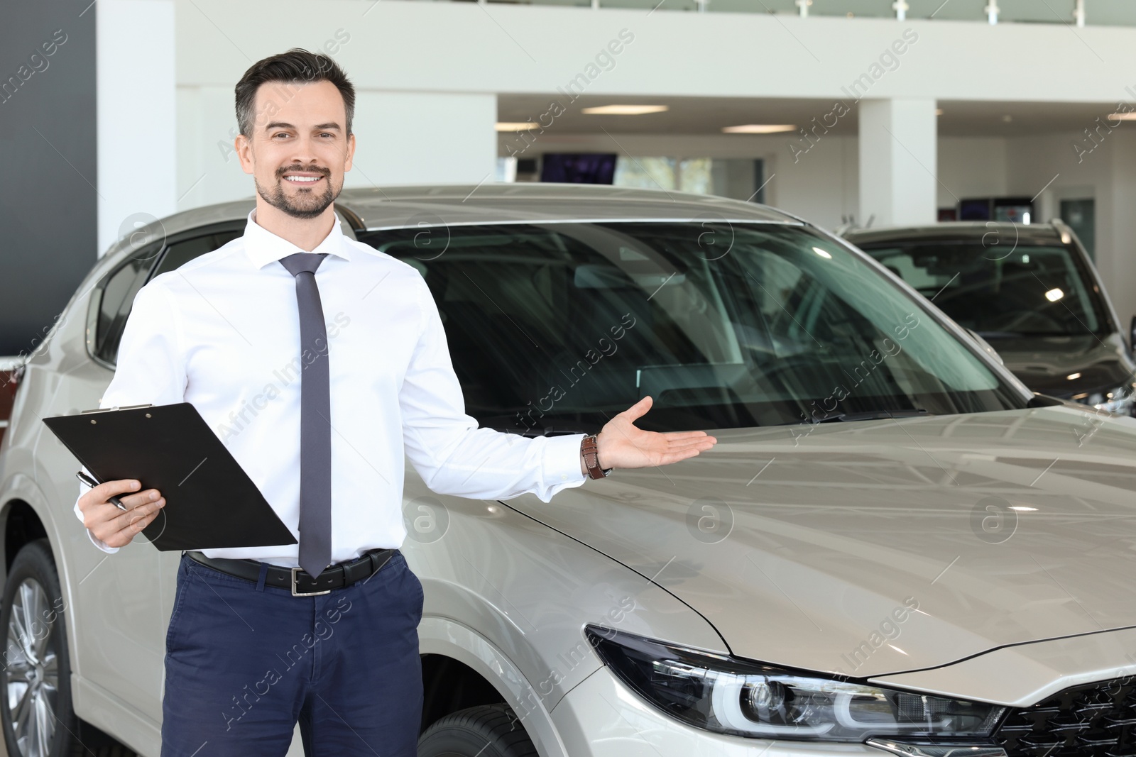 Photo of Happy salesman near new silver car in salon