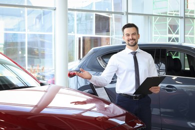 Happy salesman near new red car in salon