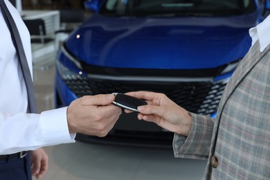 Saleswoman giving key to client near new car in salon, closeup