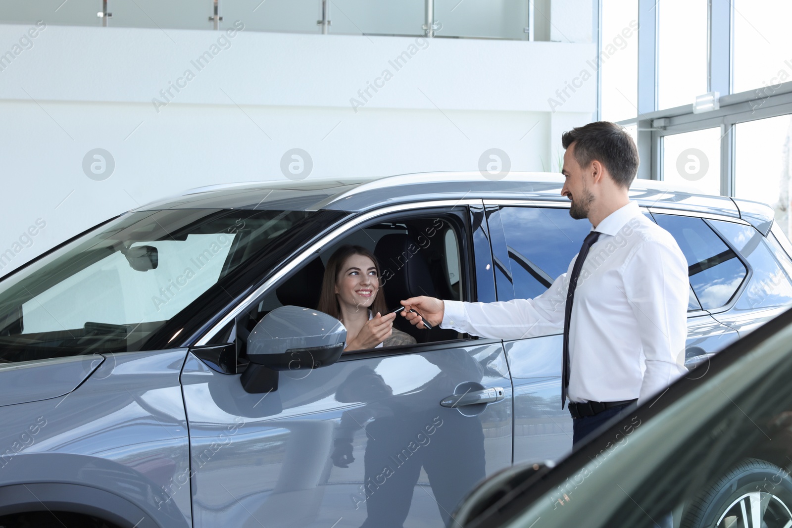 Photo of Woman giving key to man inside new car in salon