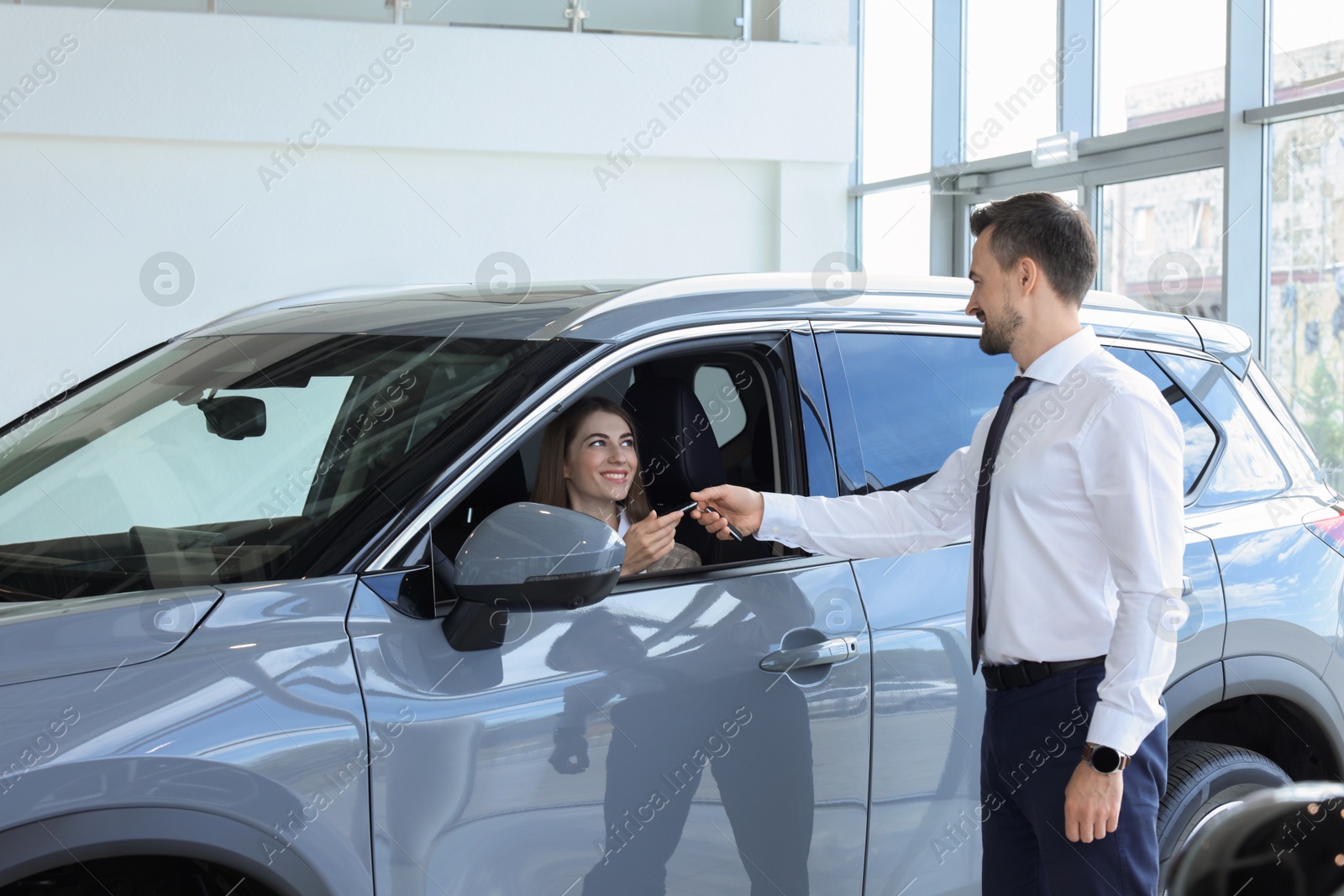 Photo of Woman giving key to man inside new car in salon