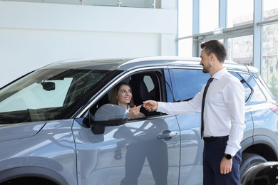 Photo of Woman giving key to man inside new car in salon