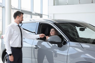 Photo of Woman giving key to man inside new car in salon