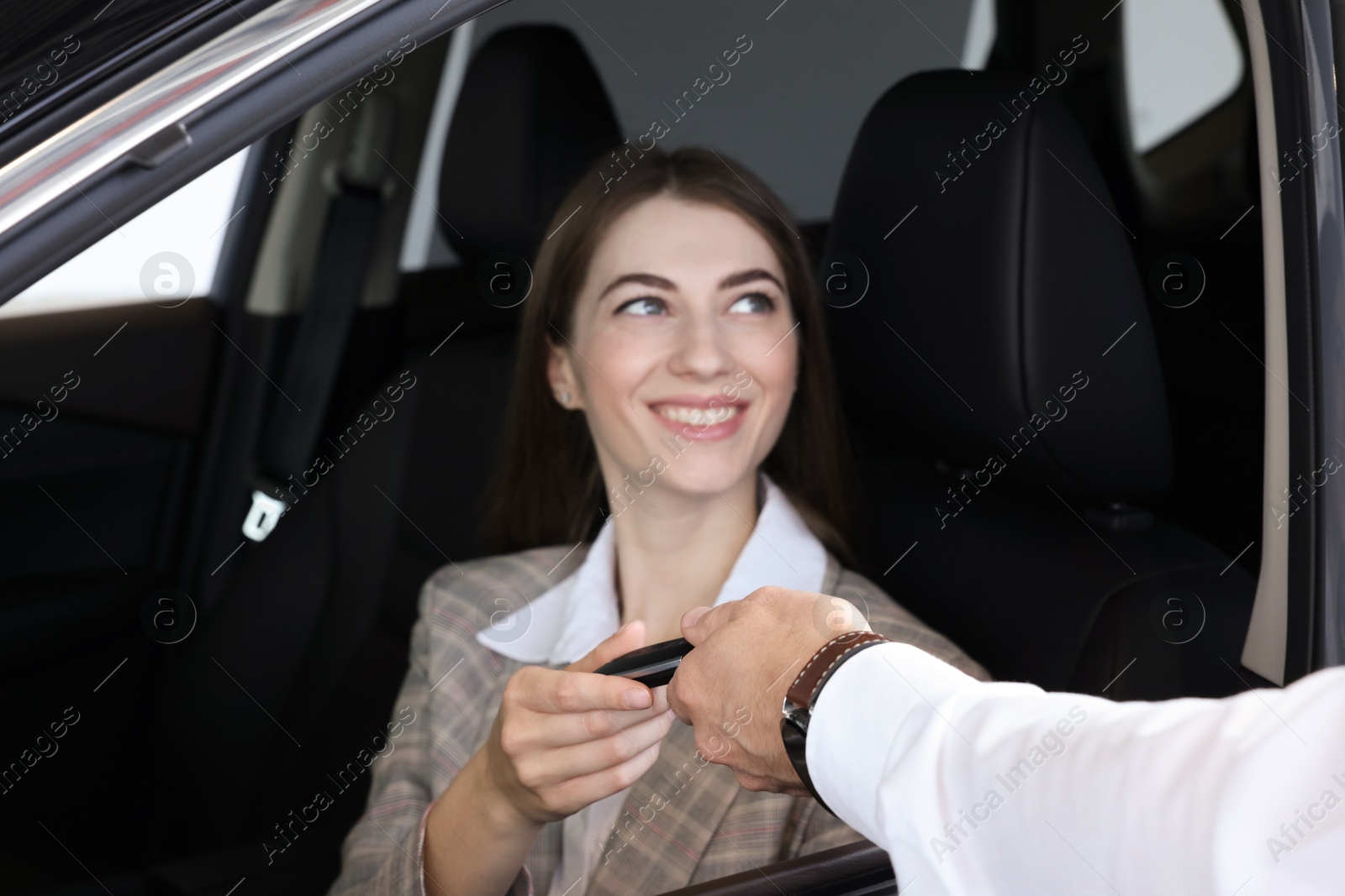 Photo of Salesman giving key to client inside new car in salon