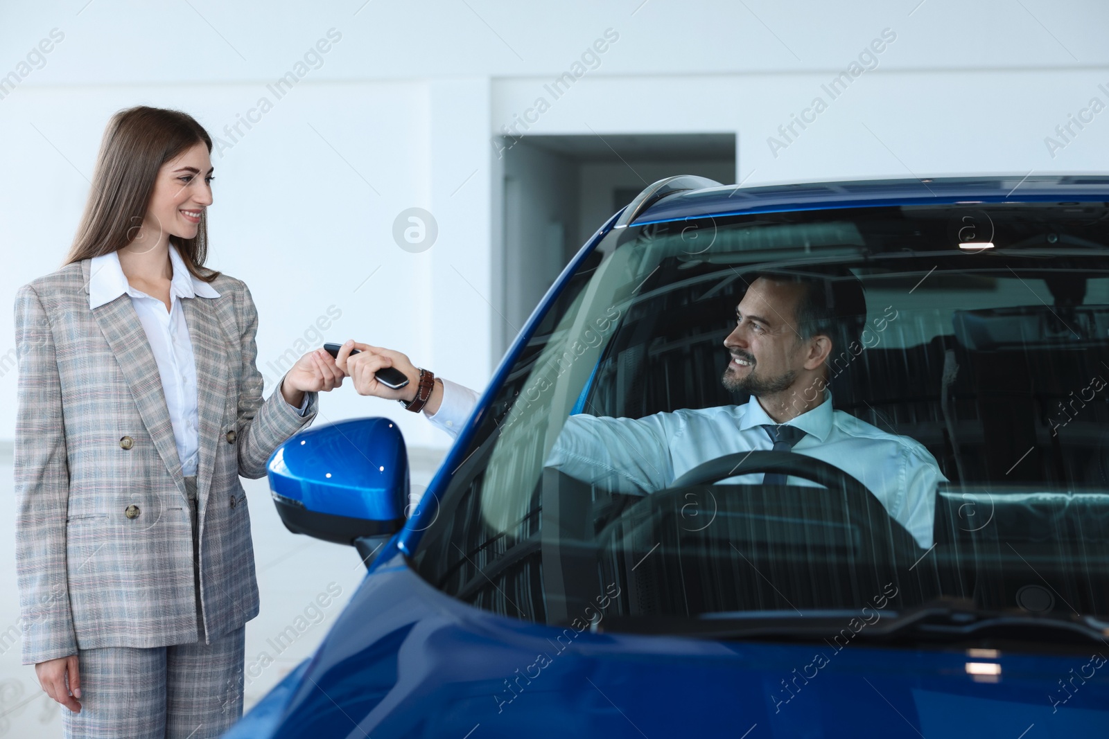 Photo of Saleswoman giving key to client inside new car in salon