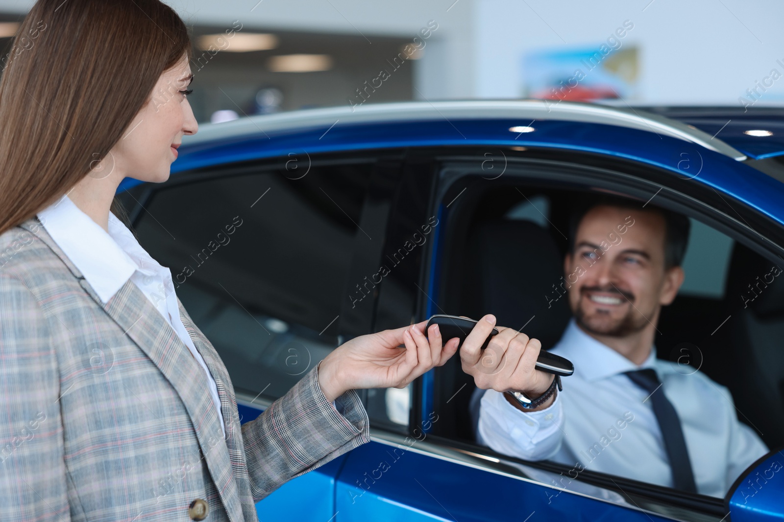 Photo of Saleswoman giving key to client inside new car in salon, selective focus